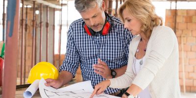 Portrait Of Male Architect And Mature Woman Discussing Plan On Blueprint At Construction Site